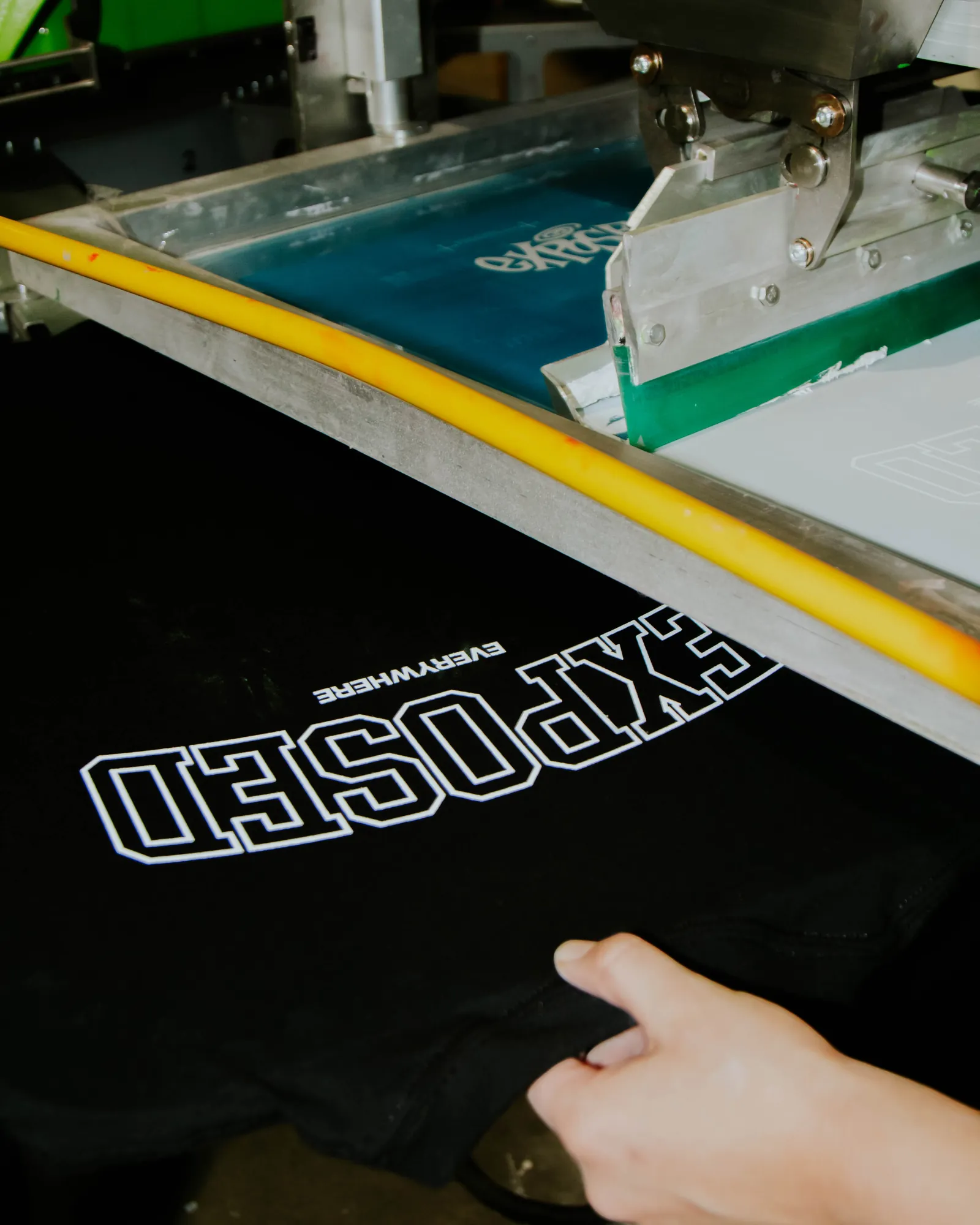 Black custom t-shirt with white EXPOSED EVERYWHERE print sitting on the press platen