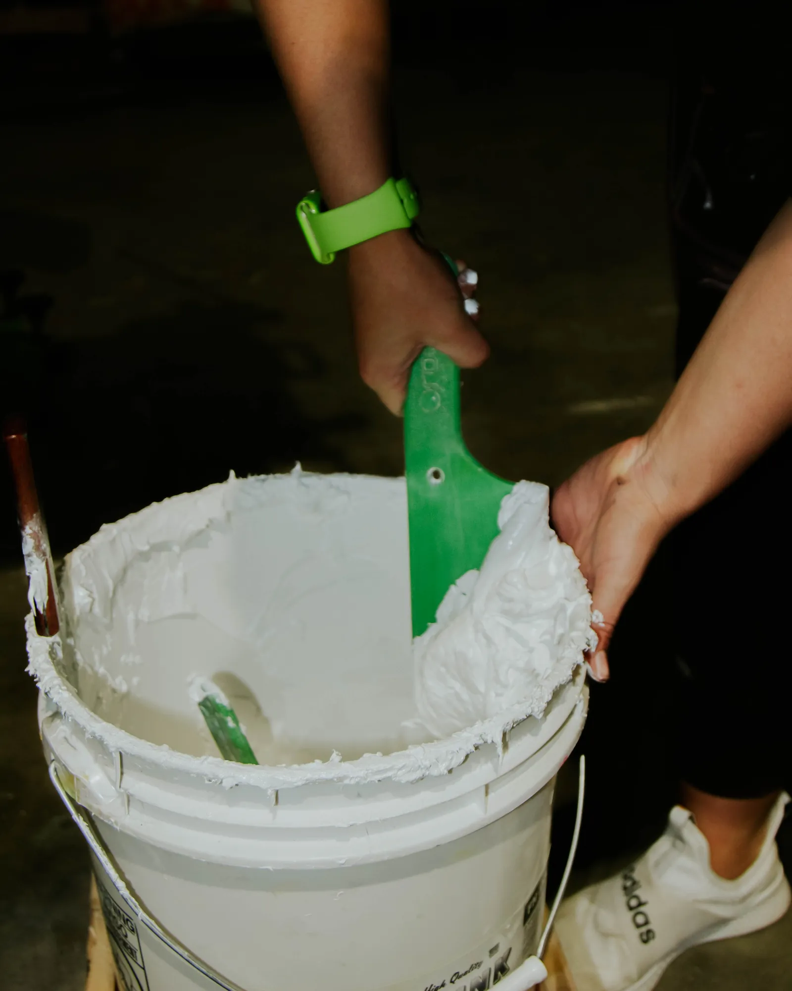 Scooping thick white plastisol ink from the bucket before a screen printing run