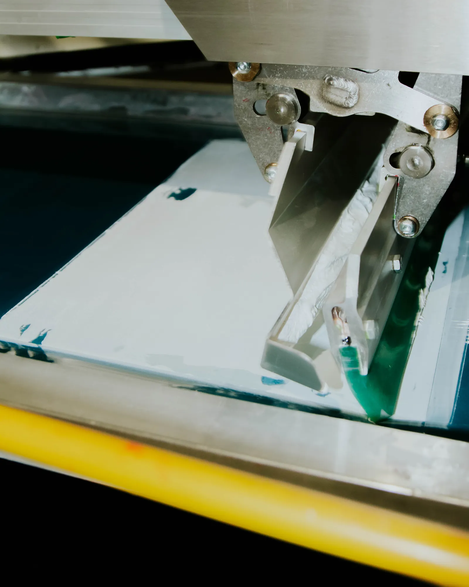 Closeup of a squeegee and press head mid-pull on the screen printing press