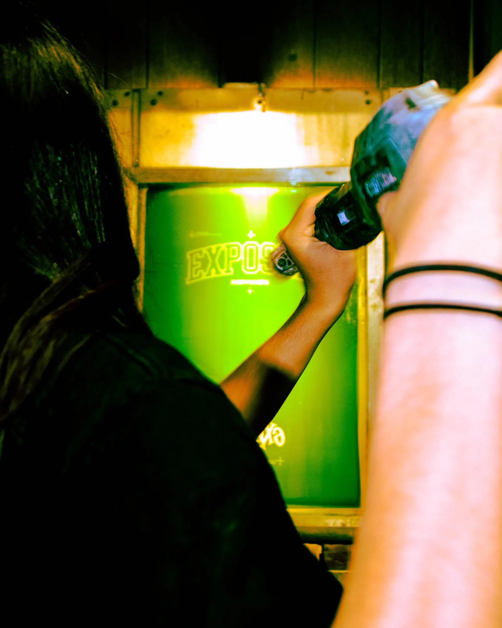 Screen burning under green UV light in the exposure unit at Fully Exposed Graphics — the screen printing step the Albuquerque shop is named for