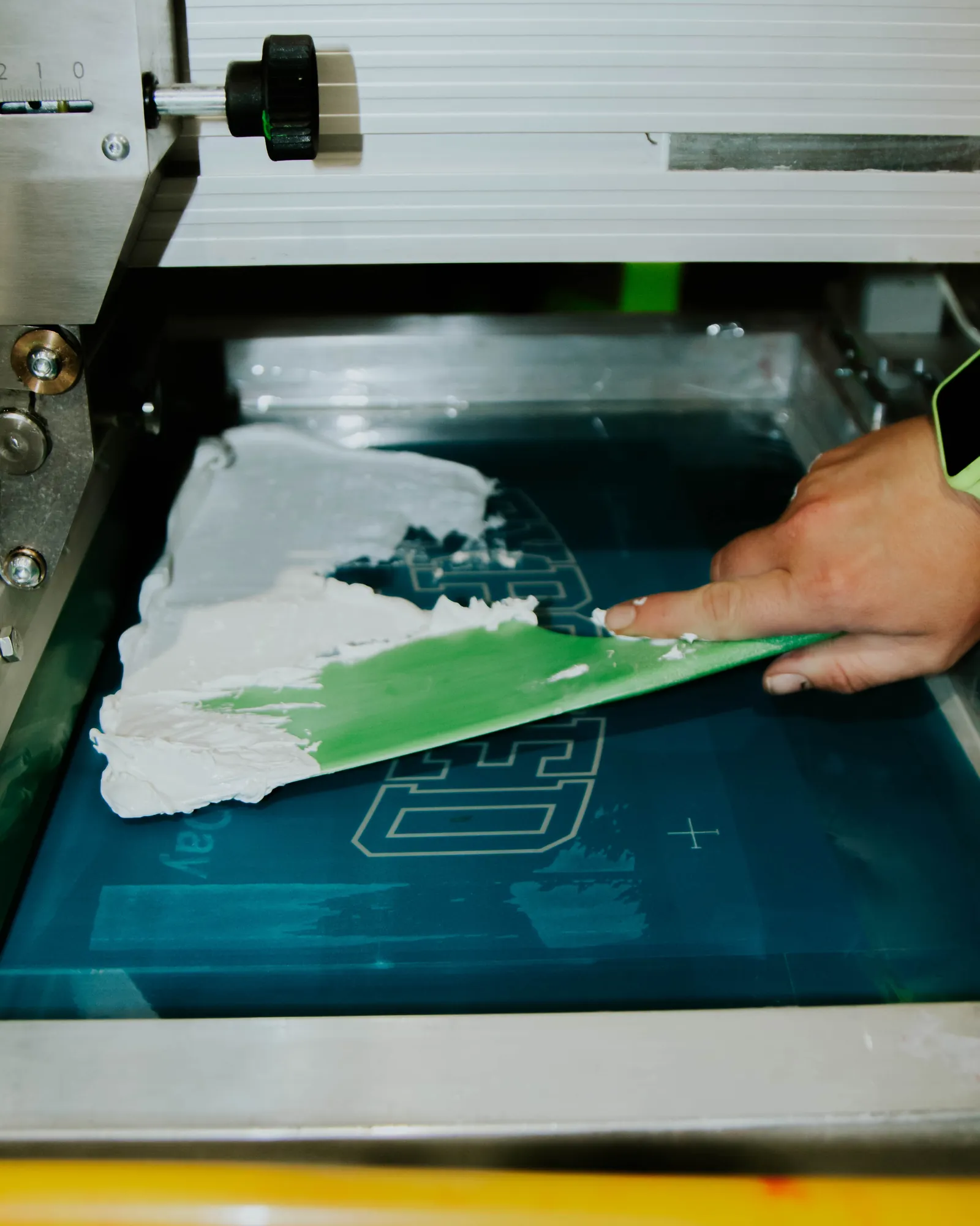 White plastisol ink being flooded across a screen ahead of the print stroke